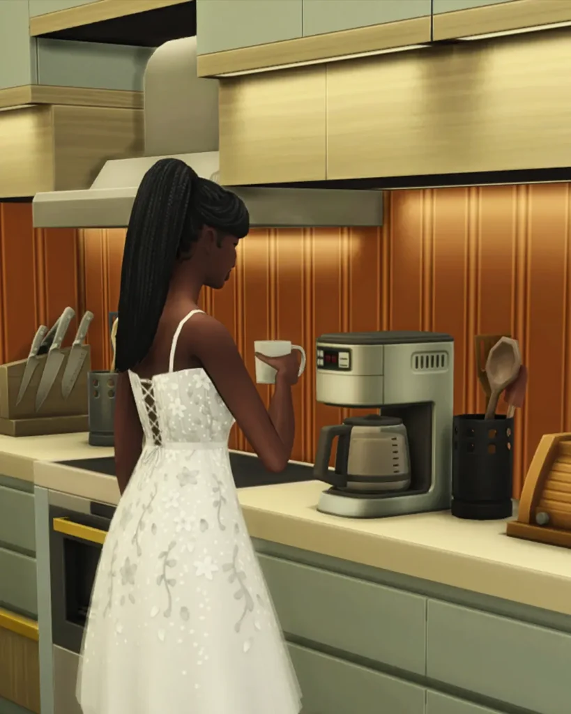 Sims 4 cc pack Sim in a white dress holding a coffee mug next to a functional CC coffee maker on a kitchen counter with sage green cabinets and copper backsplash